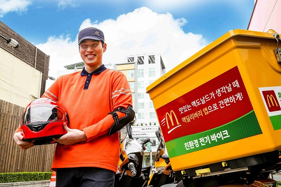 맥도날드 배달 유니폼을 입은 직원이 헬멧을 들고 배달 오토바이 옆에서 미소짓는 모습